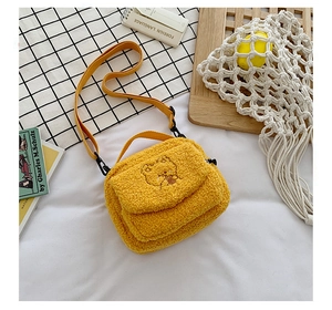 Detailed view of yellow plush messenger bag with embroidered cartoon bear and flap closure