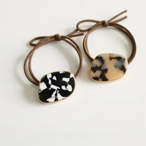 Close-up of elegant hair ties featuring marble and tortoiseshell resin oval pendants