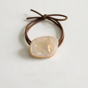 Detail of elegant handmade hair tie featuring pearl resin charm with gold edge on dark cord