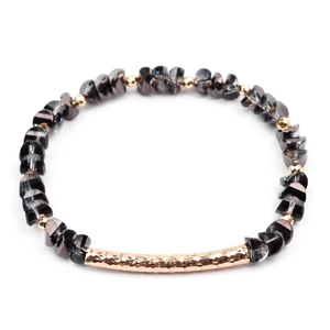 Close-up of faceted dark grey crystal beads and hammer-textured gold tube on a bracelet