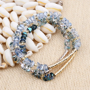 Mehrlagiges facettiertes Kristallperlenarmband mit Goldröhren auf weißen Muscheln