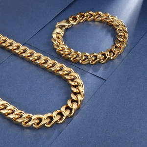 Détail d'un collier et d'un bracelet gourmette dorés sur un support texturé bleu ciel