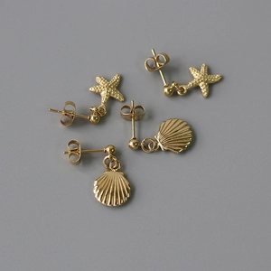 Detail of 14K gold plated starfish and seashell stud earrings on a dark grey surface