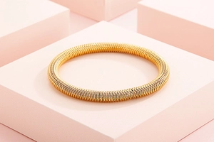 Detail of golden flexible spring mesh bangle on pink geometric blocks with metallic texture