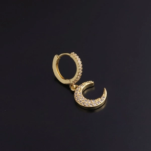 Detail of golden geometric moon earring with clear zircon inlay on a dark background