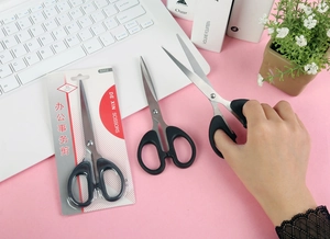Close-up of stainless steel office scissors with black handles on a pink desk background