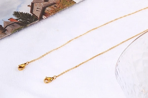 Close-up of golden stainless steel chain link necklace with lobster clasps on white surface