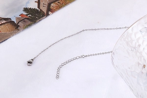 Detail view of a silver double-layer necklace with a secure spring clasp on white fabric