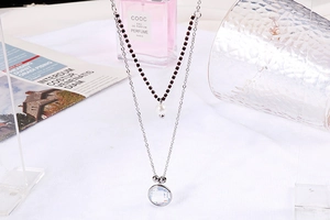 Detail of silver double-layer necklace with deep red beads and round clear pendant