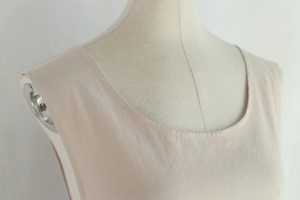 Detailed view of beige cotton apron with round neck design on a mannequin