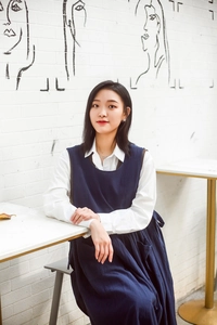 Detail of a dark blue cotton apron dress worn over a white shirt in a studio setting