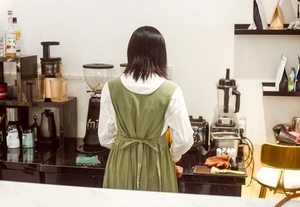 Detailed back view of olive green cotton apron with cross-back design in a cafe setting