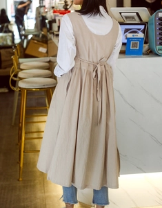 Detailed back view of a beige cotton apron dress with lace-up straps and pleated design