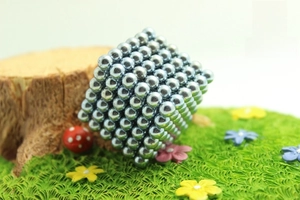 Macro shot of a silver buckyball cube made of magnetic spheres on a miniature grass lawn