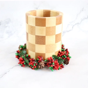 Christmas candle wreath ring with pine cones and red berries on a checkered wooden base