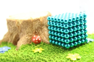Macro shot of 5mm bright blue magnetic balls formed into a cube on miniature turf