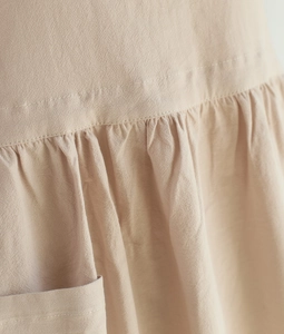 Detail view of the beige cotton apron showing waist pleats and functional pocket texture