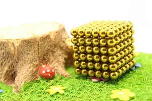 Macro detail of 5mm gold magnetic spheres arranged in a cube within a forest landscape