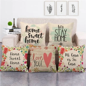 Detail of five linen cushion covers with floral patterns and quotes on a beige sofa