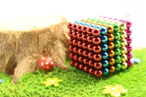 Macro shot of 216 multi-color magnetic beads arranged in a cube on a miniature grass lawn