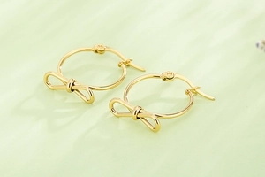 Détail de boucles d'oreilles créoles dorées en forme de nœud sur fond vert texturé