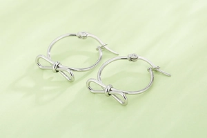 Détail de boucles d'oreilles créoles avec nœud argenté sur un fond vert pastel doux