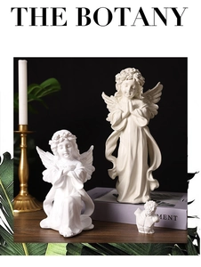 Artistic display of white resin prayer angel sculptures on a wooden table with soft lighting