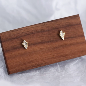 Detail view of gold geometric trapezoid stud earrings with cubic zirconia on wood