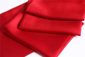 Close-up of folded red silk scarf showing smooth satin texture and elegant glossy finish