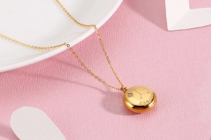 Close-up of gold stainless steel Cancer zodiac necklace with crystal on pink surface