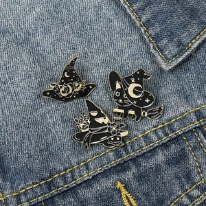 Three-piece black enamel pin set with witches, cats, and stars on blue denim jacket