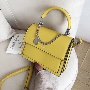 Yellow leather crossbody handbag with silver chain and fashion text on beige sofa