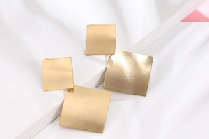 Macro shot of matte champagne gold geometric square earrings with brushed metal texture