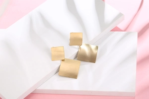 Detail of gold geometric square earrings with matte brushed texture and dual square design