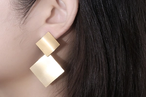 Close-up of geometric brushed gold square earrings with minimalist layered design