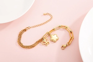 Dettaglio del bracciale dorato a catena mista con ciondoli a farfalla e stella chic