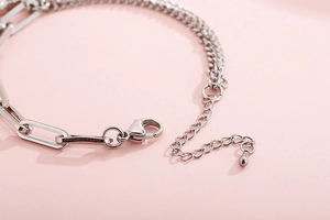 Dettaglio del bracciale a catena argentata con chiusura a moschettone e ciondolo