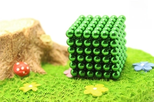 Macro detail of 216 green magnetic balls cube on a mossy creative display