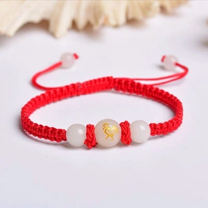 Detail of red braided bracelet with luminous white beads and golden rooster pattern