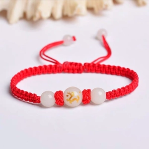 Detail of red woven cord bracelet with luminous white beads and gold dragon pattern