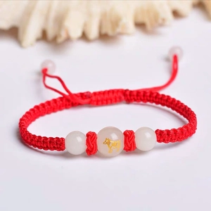 Macro detail of red woven bracelet with jade beads and golden ox zodiac engraving
