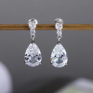 Detailed close-up of water drop cubic zirconia earrings on a minimalist wooden stand