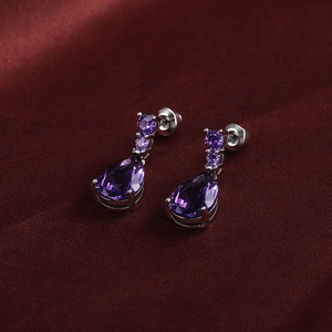 Close-up of pear-cut purple zircon earrings with silver settings on red satin