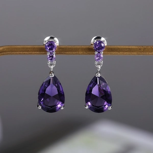 Detailed close-up of purple teardrop zircon earrings hanging on a metal jewelry display stand
