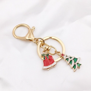 Detail of Christmas keychain with gold bell and tree charms on soft white silk background
