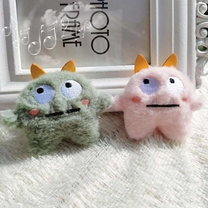 Close-up of cute green and pink plush monster pins with embroidered details and big eyes