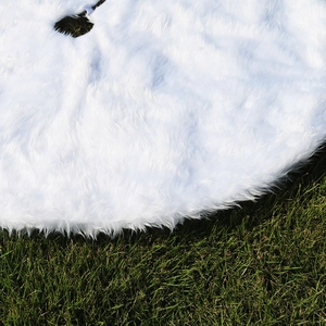 Detail of soft white faux fur Christmas tree skirt on grass showing plush texture