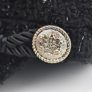 Detail of black tweed newsboy cap with vintage gold crest button and braided strap
