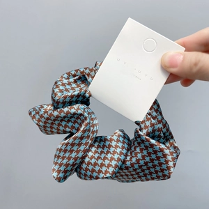 Detail of blue and brown houndstooth fabric hair scrunchie with a silky texture and tag