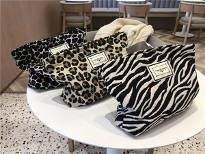 Three canvas leopard and zebra print toiletry bags arranged on a white cafe table